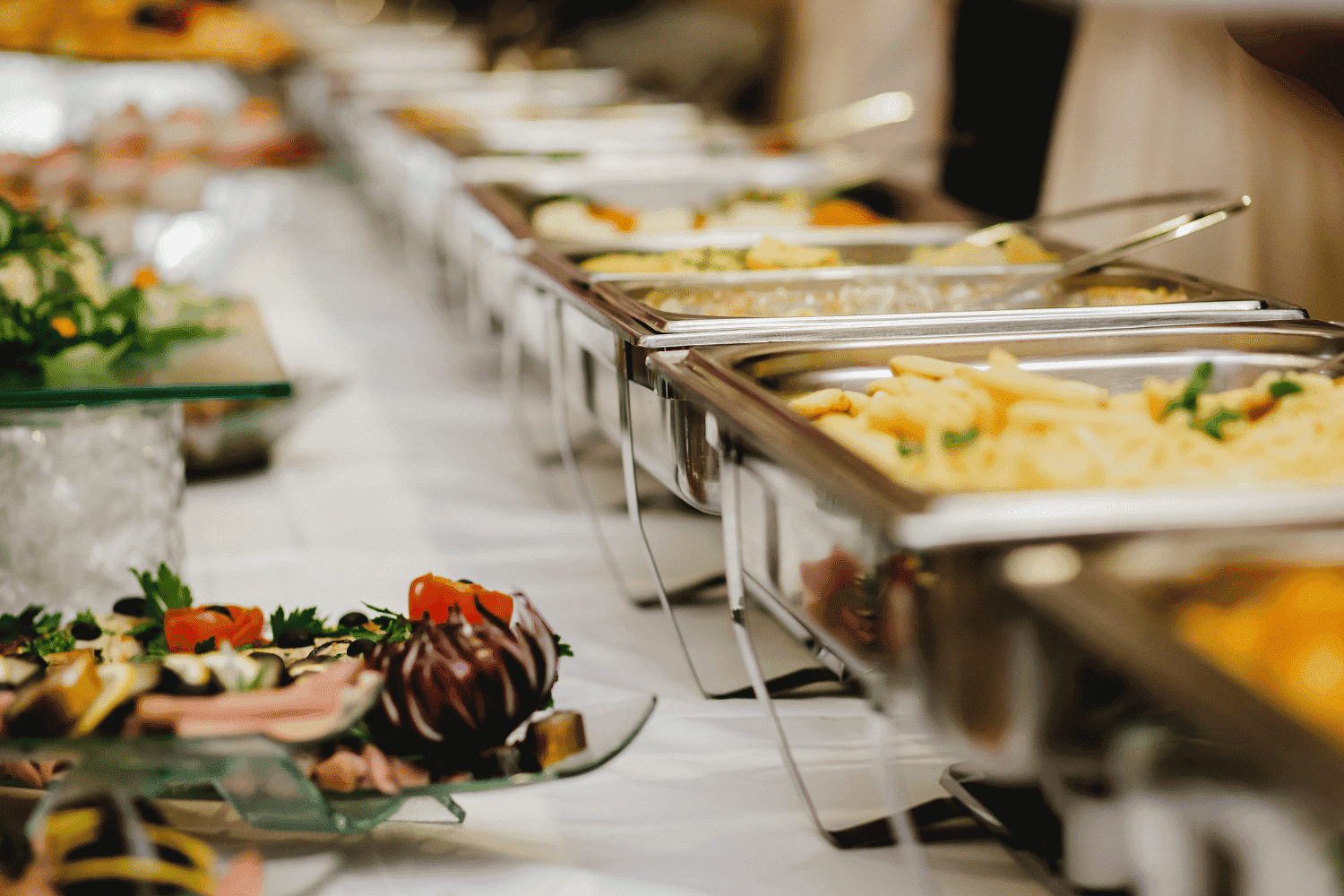 Buffet table with various dishes, including pasta and salads, on a white tablecloth.