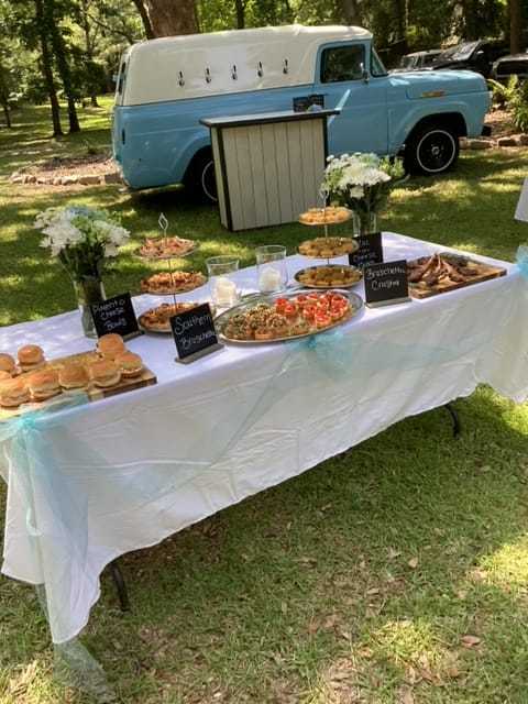Outdoor buffet setup with sandwiches, veggies, and snacks in front of a vintage blue van.